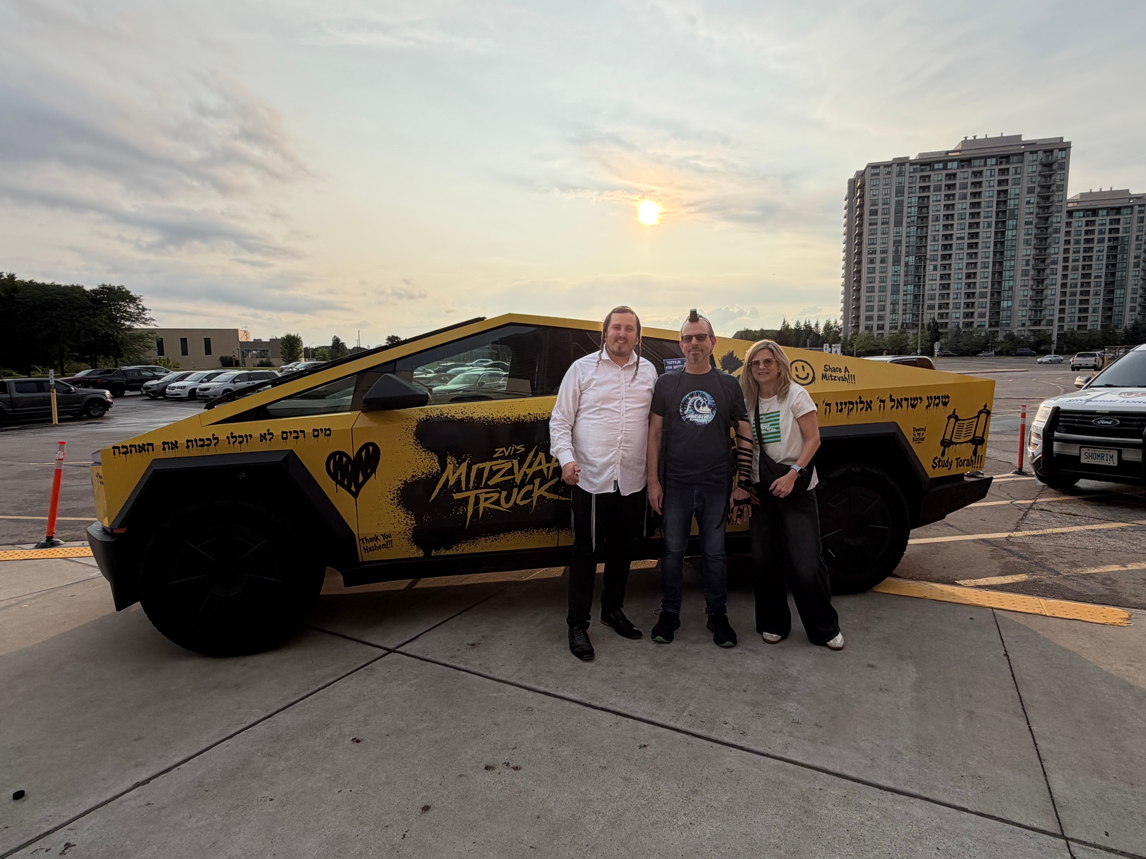 Three people posing with the Mitzvah Truck at sunset